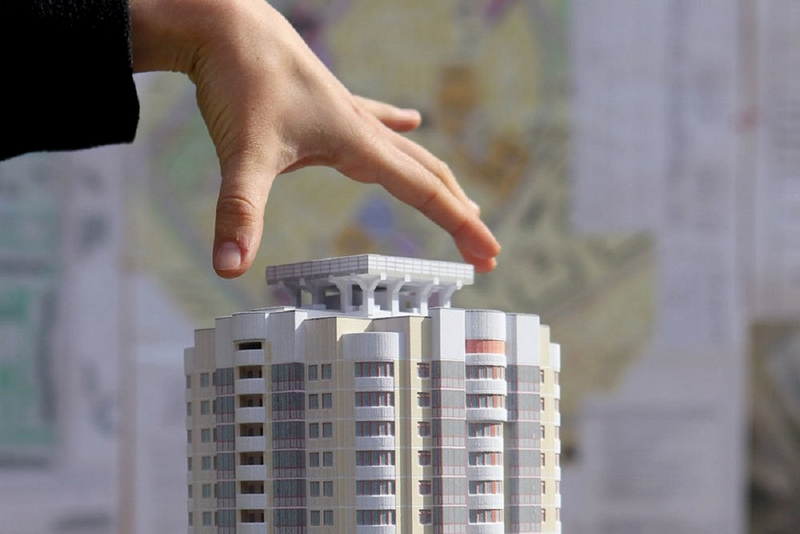 A hand adjusting the roof of a miniature model of a multi-story building.